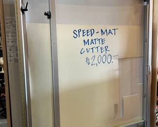 Professional Speed-Mat matte cutter designed for precision framing work. Heavy-duty metal construction with adjustable guides and cutting controls for accurate, clean mat cuts. Wall-mounted style unit suitable for framing shops, studios, or serious artists. Shows normal wear from professional use.