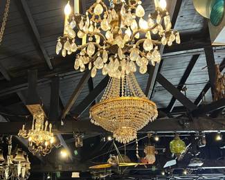 Spectacular antique crystal chandeliers suspended overhead, featuring cascading prisms, candle-style lights, and ornate metal frameworks. Multiple fixtures create a dazzling, old-world atmosphere with exceptional sparkle and presence. Ideal for grand interiors, restoration projects, or dramatic decorative display. All items sold as-is.
