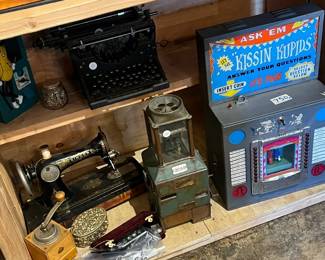 Vintage mechanical and novelty display featuring an antique sewing machine, early typewriter, metal vending or coin-operated device, and a colorful Kissin’ Koppas arcade-style machine. A lively mix of industrial, mechanical, and Americana pieces with strong visual appeal and age-earned patina. Ideal for collectors, game rooms, or theatrical display. All items sold as-is.