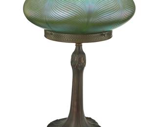 3076
A Quezal glass mushroom table lamp
Early 20th century
Marked to shade rim interior: Quezal
The green iridescent glass pulled feather shade with white interior, set on an Art Nouveau patinated metal base with foliate motifs, electrified
Overall: 19.75" H x 13.25" Dia.
Estimate: $2,000 - $3,000