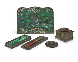 3035
Five assembled Tiffany Studios desk accessories
Early 20th century
Each stamped: Tiffany Studios New York
The patinated bronze and green slag glass items, comprising a 'Grapevine' letter rack, no. 1007 (8.75' H x 12.5' W x 3.5'D), a 'Pine Needle' pen tray (1' H x 8.5' W x 3' D), a 'Zodiac' pen tray, no. 1000 (9.75" W x 3.125" D), a 'Grapevine' inkwell, no. 844, with glass liner (3.5' H x 4' W x 4' D), and a 'Pine Needle' blotter (1.25' H x 3.25' Dia.), together with an associated letter opener
6 pieces
Estimate: $600 - $800