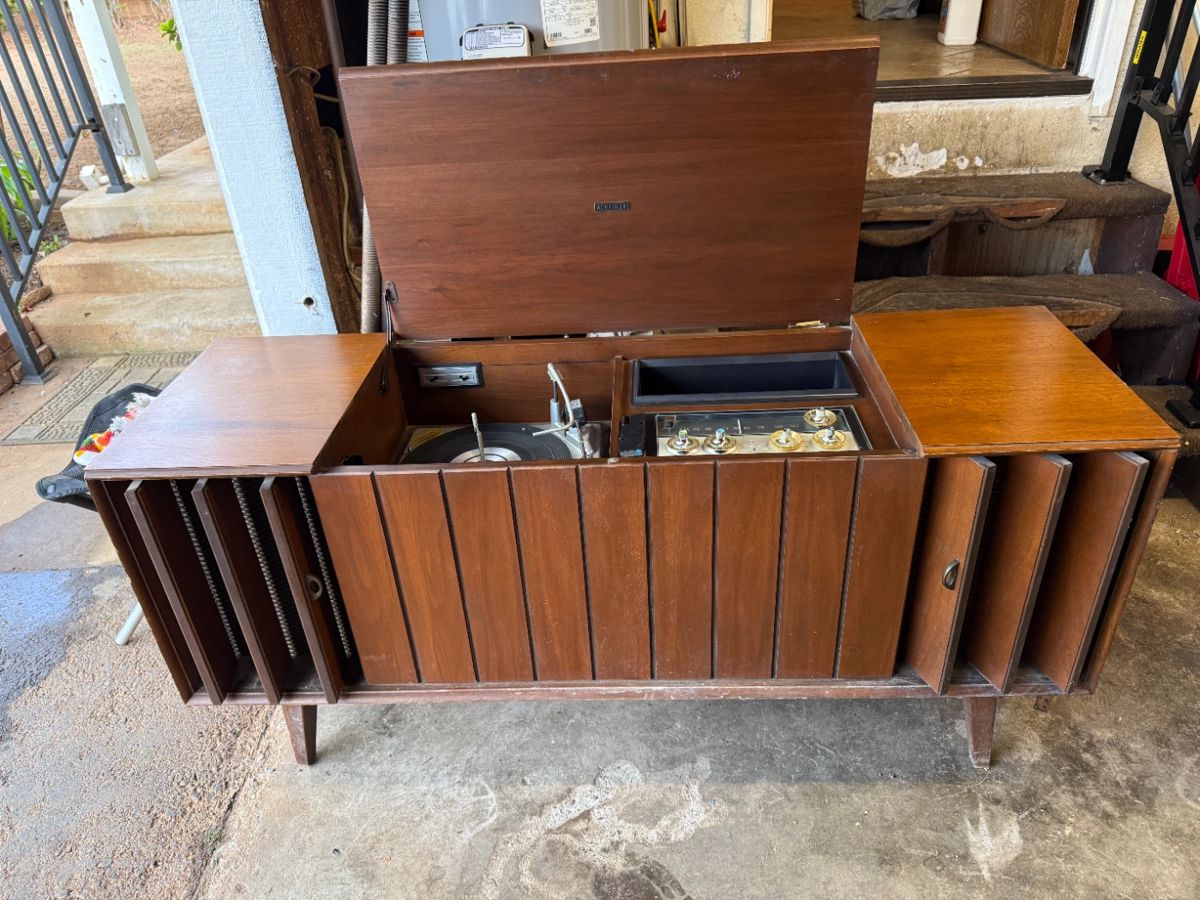 This is a mid-century modern Zenith solid-state stereo console in a walnut finish.
The console features a built-in record player and AM/FM radio.
It has louvered doors that conceal the speakers and record storage compartments.
Many Zenith consoles from this era, including models like the MN2604, are sought after by collectors for their stylish appearance and quality components.
The record player often features the Micro-Touch 2G tonearm, known for its light tracking force.