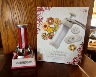 This is a Wilton Cookie Max cookie press. 
It uses an easy pump action, with one click of the plunger producing one cookie. 
The press comes with 12 different shape disks, including classic spritz cookie shapes like trees, stars, and flowers. 
For best results, use an ungreased non-stick cookie sheet to prevent the dough from spreading or sticking. 
The item is priced at $14.99, as shown on the box. 
