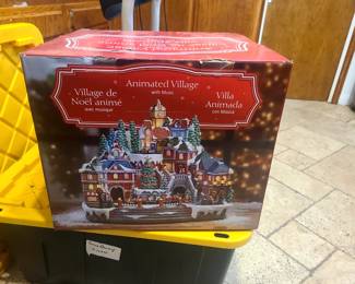 The image shows a box for a Kirkland Signature or Moments in Time Animated Christmas Village with Music, likely sold at Costco. 
The village is animated, plays eight different Christmas songs, and features LED lighting. 
It includes a rotating fea