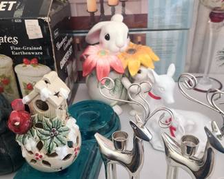 The image features several decorative items, including a set of silver reindeer candle holders and a ceramic birdhouse-shaped candle holder, which appear to be collectibles. 
The silver reindeer candle holders are designed for taper or votive candles.
They feature a minimalist design, with the antlers forming the holders.
The ceramic birdhouse features a holly and berry motif, suggesting a Christmas or winter holiday theme.
Also visible is a ceramic bunny figurine with flower decorations.
A box for an "ET C