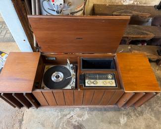This is a mid-century modern Zenith solid-state stereo console in a walnut finish. 
The console features a built-in record player and AM/FM radio. 
It has louvered doors that conceal the speakers and record storage compartments. 
Many Zenith consoles from this era, including models like the MN2604, are sought after by collectors for their stylish appearance and quality components. 
The record player often features the Micro-Touch 2G tonearm, known for its light tracking force. 
