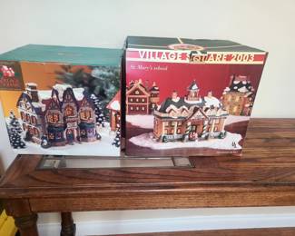 These are Mervyn's Village Square ceramic Christmas village houses from the 1990s and early 2000s. 
The boxes indicate they are part of a collectible series. 
The box on the right is specifically labeled as "St. Mary's school" from the "Village Square 2003" collection.
The one on the left is a similar style of lighted building, likely from a different year in the same collection.
These are desi