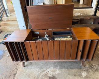 This is a mid-century modern Zenith solid-state stereo console in a walnut finish.
The console features a built-in record player and AM/FM radio.
It has louvered doors that conceal the speakers and record storage compartments.
Many Zenith consoles from this era, including models like the MN2604, are sought after by collectors for their stylish appearance and quality components.
The record player often features the Micro-Touch 2G tonearm, known for its light tracking force.
