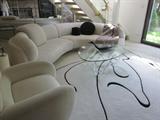 Contemporary sofa and chair, rug is cut and sculpted to fit and flow around the furniture. Glass top table