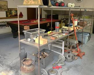 On these shelves you can see a variety of objects, including a floor jack, weightlifting weights, a table-model drill press, a crow, a bowling ball, and other items.
