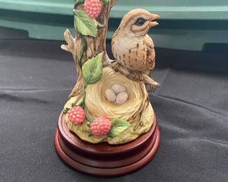 a small bird perched next to a nest with eggs and raspberry decorations.
