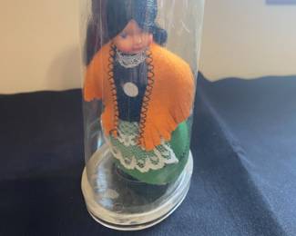 vintage hard plastic doll, possibly an Irish souvenir doll, is fixed to the base of its display case.