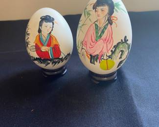 vintage hand-painted Chinese eggs, typically depicting ladies in a garden scene, displayed on small lacquered wood stands.
