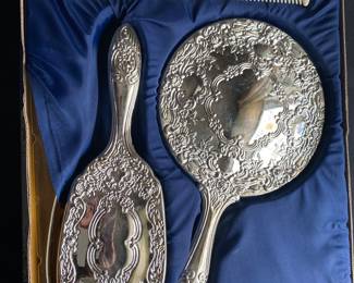 a vintage silver-plated three-piece vanity set, including a hand mirror, hairbrush, and comb.