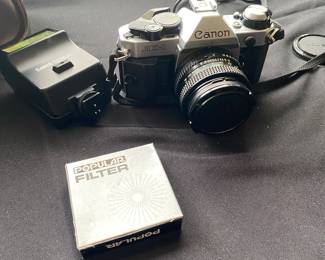 a vintage Canon AE-1 35mm SLR film camera with a flash attachment and a "Popular Filter" accessory box