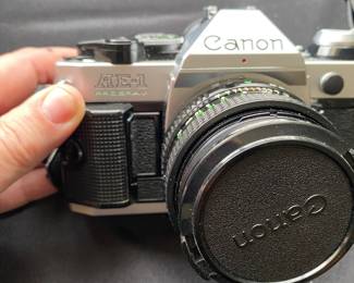 a vintage Canon AE-1 35mm SLR film camera with a flash attachment and a "Popular Filter" accessory box