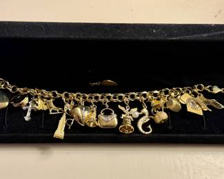 14K Gold Bracelet with charms including a locket, a cross, an ice skate, a frog, the Empire State Building, a heart, a handbag embellished with small diamonds, a bell with an eagle and pearl, a seahorse, a teapot, and the US flag.