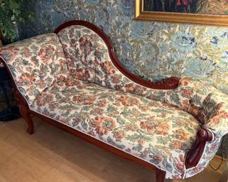 vintage or antique Victorian-style fainting couch or chaise lounge with ornate carved wood legs and floral upholstery.