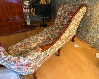 vintage or antique Victorian-style fainting couch or chaise lounge with ornate carved wood legs and floral upholstery.