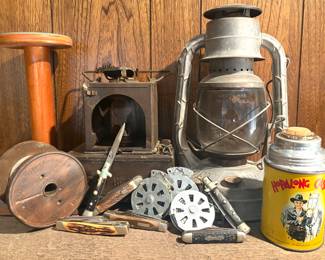 A collection of vintage items, including an antique oil lantern made by Dietz, Hopalong Cassidy themed thermos, a small stove, knives, and bank lines.  