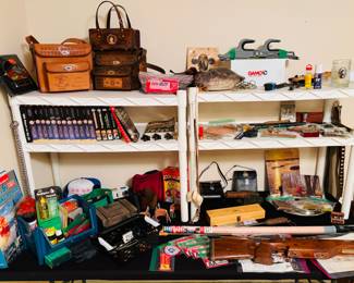 A collection of various outdoor activities, including hunting, and fishing. 
several leather bags/purses, a taxidermied fish, various small tools and accessories. A white and blue baseball cap, a wooden box, and a wooden rifle. 