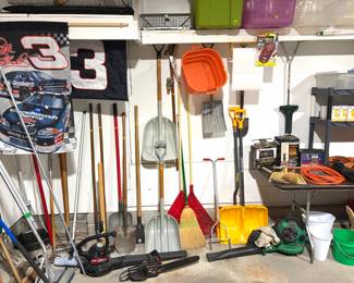 Garage tools: shovels, brooms, two electric leaf blowers, and a chainsaw.