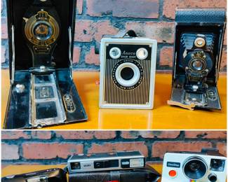Vintage Kodak No. 2 Folding Autographic Brownie camera, vintage Ansco Shur-Shot box camera, vintage Kodak No. 2 Folding Autographic Brownie camera, Olympus Stylus 35mm compact film camera, Minolta Pocket Autopak 460TX 110 film camera, a red Samsung WB35F Smart Digital Camera and a vintage Polaroid SX-70 OneStep Land Camera. 