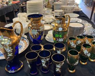 Collection of Czechoslovakian cobalt glass featuring deep blue and emerald green pieces with gold gilt and hand-painted floral decoration. Includes vases, pitchers, and matching drinking glasses. Elegant European glassware ideal for display or use, with rich color and decorative detailing throughout.