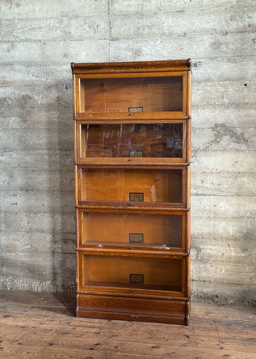 This lot features a stacking barrister bookcase manufactured by Globe Wernicke, dating back to the early 1900s. This bookcase in particular has a total of seven (7) pieces – 5 stacking bookcases, a base, and a topper. This piece measures from top to bottom, 75” H x 34” W x 11” D.