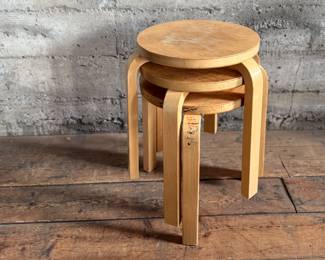 This lot features a set of three Artek Nesting Stools (model E60) in natural birch veneer, designed by Alvar Aalto. Each stool measures, 17” H x 13.5” W x 13.5” D. Designed by Alvar Aalto in 1933, the stools are a classic of Finnish modernism. They feature a patented L-shaped bent-leg construction, which makes them sturdy and easily stackable. 

