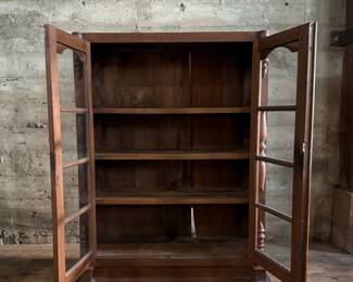 This lot features an early antique cherry wood display cabinet or bookcase. Two pieces (base is separate) with locking doors and skeleton key included. One glass pane is missing and some trim could be reattached that is included. This piece measures, 56.25” H x 42” W x 16.5” D.

