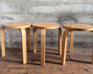 This lot features a set of three Artek Nesting Stools (model E60) in natural birch veneer, designed by Alvar Aalto. Each stool measures, 17” H x 13.5” W x 13.5” D. Designed by Alvar Aalto in 1933, the stools are a classic of Finnish modernism. They feature a patented L-shaped bent-leg construction, which makes them sturdy and easily stackable. 

