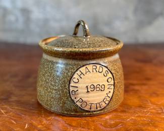This lot features a lidded crock or jar by Richards Pottery, dated 1969. A wonderful example of studio pottery made of stoneware material and features a speckled brown glaze. This crock measures, 5” H x 6” W x 6” D.

