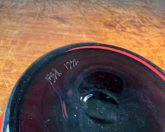 This lot features a stunning postmodern art glass bowl by IBEX Glass Studio circa 1992. This bowl is in excellent condition, signed underneath, and measures, 8” H x 13” W x 13” D. Formed in 1985 by Dimitri Michaelides, Sam Stang and David Levi, IBEX Glass Studio was heavily influenced by American studio glass pioneers, mid-century Venetian glass, and postmodern European design, including Ettore Sottsass and his Memphis contemporaries. Sitting on a round black foot, this bowl has a tapered cylindrical red bowl, and a delicate yellow rim.

