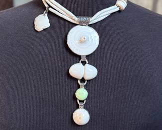 This lot features a special custom necklace by listed designer, Melanie DeLuca. Engraved sterling silver with shells & stones throughout. This piece measures, 17” and has a total approx. weight of 193.49 grams. Melanie DeLuca’s bold jewelry designs of mixed media, plastics and ethnographic objects embody a celebration of her 45 years as a metalsmith, jewelry designer and master teacher. Her interest in jewelry design began early and solidified at 17. By 20, she was apprenticing for master silversmith Brooks Darrow (himself an apprentice of renowned English architect and master metalsmith Louis Osman). Early work in painting and sculpture informed Melanie’s growing connection to the limitless expression of metal through jewelry design and fabrication.

