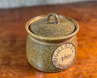 This lot features a lidded crock or jar by Richards Pottery, dated 1969. A wonderful example of studio pottery made of stoneware material and features a speckled brown glaze. This crock measures, 5” H x 6” W x 6” D.

