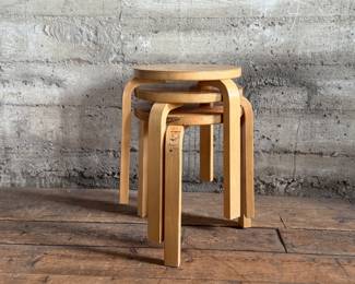 This lot features a set of three Artek Nesting Stools (model E60) in natural birch veneer, designed by Alvar Aalto. Each stool measures, 17” H x 13.5” W x 13.5” D. Designed by Alvar Aalto in 1933, the stools are a classic of Finnish modernism. They feature a patented L-shaped bent-leg construction, which makes them sturdy and easily stackable. 

