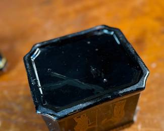 This lot features an antique English tea caddy, attributed to Henry Clay circa 1850s. It features classical Etruscan-style figures and borders with the top decorated with a reclining dog figure. This caddy measures, 5.5” H x 4.5” W x 3.5” D.

