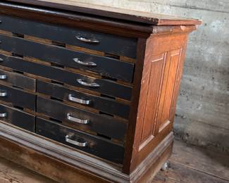 This lot features a vintage solid wood apothecary style or print maker’s cabinet. Comes on casters with multiple sized pull out drawers. The top "lift up" board is currently not attached to the backside trim, but can be easily fixed or left as is. The top cabinet area has green felt. This cabinet measures, 33.25” H x 46” W x 23” D.

