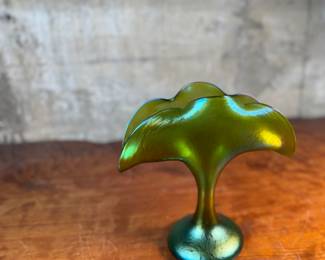 This lot features an Art Nouveau iridescent green art glass vase, likely produced by Loetz or Pallme-König between approximately 1890 and 1919. This vase measures, 9.75” H x 9.5” W x 5” D.

