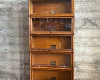 This lot features a stacking barrister bookcase manufactured by Globe Wernicke, dating back to the early 1900s. This bookcase in particular has a total of seven (7) pieces – 5 stacking bookcases, a base, and a topper. This piece measures from top to bottom, 75” H x 34” W x 11” D.


