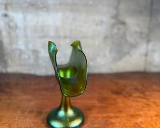 This lot features an Art Nouveau iridescent green art glass vase, likely produced by Loetz or Pallme-König between approximately 1890 and 1919. This vase measures, 9.75” H x 9.5” W x 5” D.

