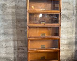 This lot features a stacking barrister bookcase manufactured by Globe Wernicke, dating back to the early 1900s. This bookcase in particular has a total of seven (7) pieces – 5 stacking bookcases, a base, and a topper. This piece measures from top to bottom, 75” H x 34” W x 11” D.

