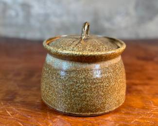 This lot features a lidded crock or jar by Richards Pottery, dated 1969. A wonderful example of studio pottery made of stoneware material and features a speckled brown glaze. This crock measures, 5” H x 6” W x 6” D.

