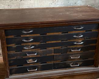 This lot features a vintage solid wood apothecary style or print maker’s cabinet. Comes on casters with multiple sized pull out drawers. The top "lift up" board is currently not attached to the backside trim, but can be easily fixed or left as is. The top cabinet area has green felt. This cabinet measures, 33.25” H x 46” W x 23” D.

