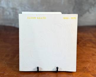 This lot features a rare book on the renowned, Alvar Aalto. Includes additional items in book, including Aalto’s exhibit pamphlet from the Mt. Angel Abbey show in 1980. Alvar Aalto (1898-1976) was a world-renowned Finnish architect, designer, and town planner, a key figure in Modernism, celebrated for his humanist approach blending functional design with organic forms and natural materials, leaving a legacy in buildings like Paimio Sanatorium and furniture like the Artek stools.

