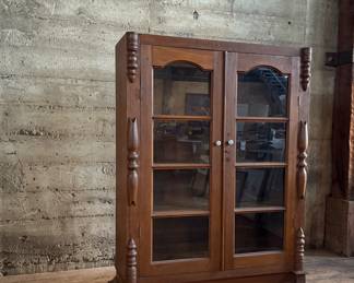 This lot features an early antique cherry wood display cabinet or bookcase. Two pieces (base is separate) with locking doors and skeleton key included. One glass pane is missing and some trim could be reattached that is included. This piece measures, 56.25” H x 42” W x 16.5” D.


