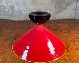 This lot features a stunning postmodern art glass bowl by IBEX Glass Studio circa 1992. This bowl is in excellent condition, signed underneath, and measures, 8” H x 13” W x 13” D. Formed in 1985 by Dimitri Michaelides, Sam Stang and David Levi, IBEX Glass Studio was heavily influenced by American studio glass pioneers, mid-century Venetian glass, and postmodern European design, including Ettore Sottsass and his Memphis contemporaries. Sitting on a round black foot, this bowl has a tapered cylindrical red bowl, and a delicate yellow rim.

