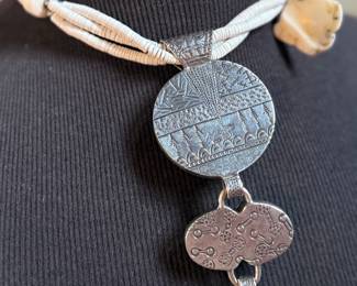 This lot features a special custom necklace by listed designer, Melanie DeLuca. Engraved sterling silver with shells & stones throughout. This piece measures, 17” and has a total approx. weight of 193.49 grams. Melanie DeLuca’s bold jewelry designs of mixed media, plastics and ethnographic objects embody a celebration of her 45 years as a metalsmith, jewelry designer and master teacher. Her interest in jewelry design began early and solidified at 17. By 20, she was apprenticing for master silversmith Brooks Darrow (himself an apprentice of renowned English architect and master metalsmith Louis Osman). Early work in painting and sculpture informed Melanie’s growing connection to the limitless expression of metal through jewelry design and fabrication.

