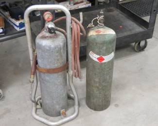 Lot 105. Two older Acetylene tanks, one gauge, small torch, and a wrench included, plus a cart